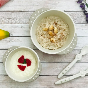 A large bowl contains oatmeal and diced banana top with cinnamon powder.  A small bowl contains plain yogurt and raspberries.