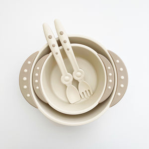 A 8 ounce beige bowl is in a 16 oz beige bowl. Stay clean baby spoon and fork are in the bowls with side handles.